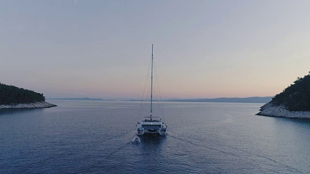 宁静的航拍双体游艇驶出美丽的海湾。这是傍晚天空与粉红色和热带海岸可见的色调。