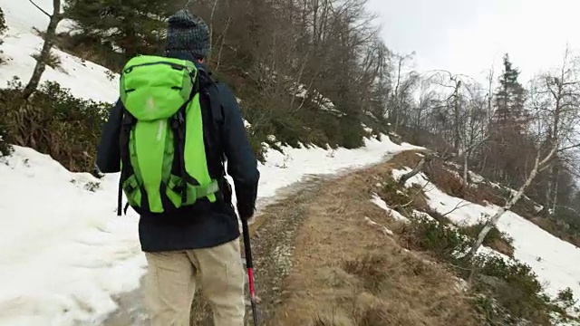 背包男徒步行走在雪道上。跟随在后面。真正的背包客成人徒步旅行或徒步旅行在秋冬野外野外的山区自然，大雾天气恶劣。4 k的视频