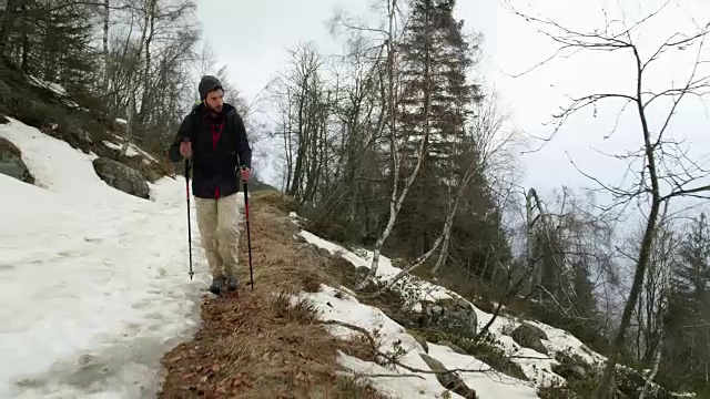 背包男徒步行走在雪道上。在前面。真正的背包客成人徒步旅行或徒步旅行在秋冬野外野外的山区自然，大雾天气恶劣。4 k的视频