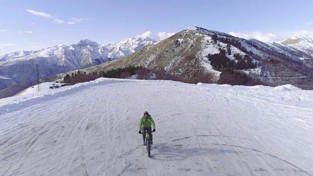 向后空中俯瞰骑着MTB电动车的人在冬天的雪道上骑车。冬天在户外雪地上骑自行车。4k无人机飞行视频