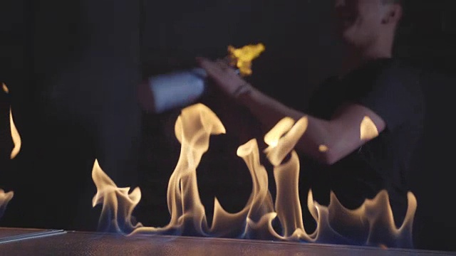 调酒师在一个流动酒吧里摆弄燃烧的瓶子，前景是火