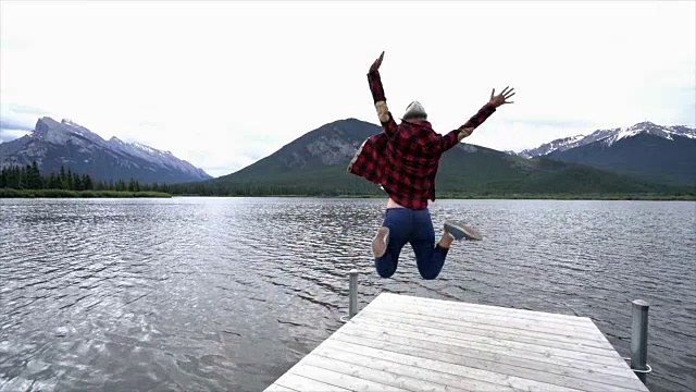 年轻女子在山湖边半空中跳着