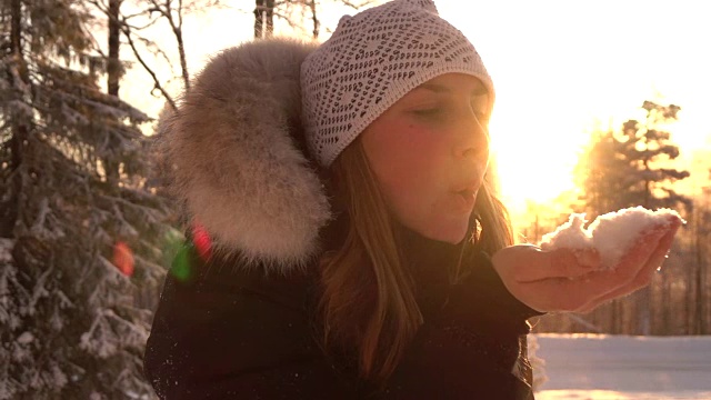 慢镜头:在神奇的冬天，年轻女子在夕阳下吹着雪花