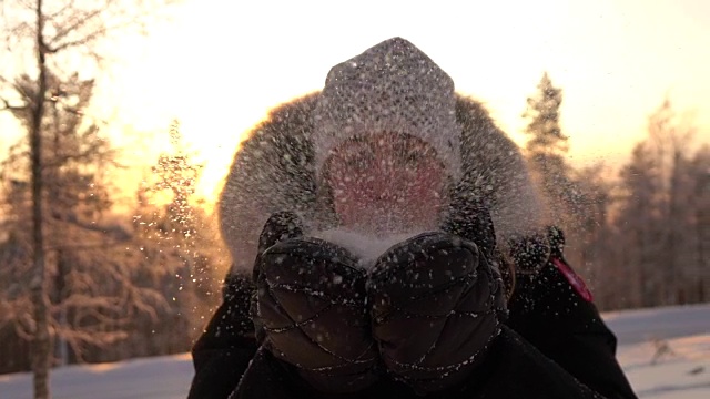 慢镜头:在神奇的冬天，年轻女子在夕阳下吹着雪花