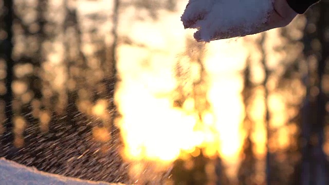 慢镜头:日落时分，双手捧起新鲜柔软的雪花飘落下来