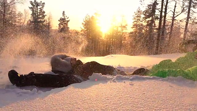 慢镜头:金色的夕阳下，快乐的女孩在山上的雪地里制作雪天使