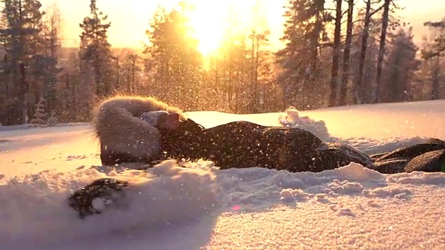 慢动作顽皮的女孩在金色的夕阳下在新鲜的雪中制造雪天使