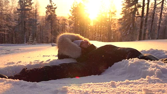 詳情圖-慢動(dòng)作頑皮的女孩在金色的夕陽(yáng)下在新鮮的雪中制造雪天使