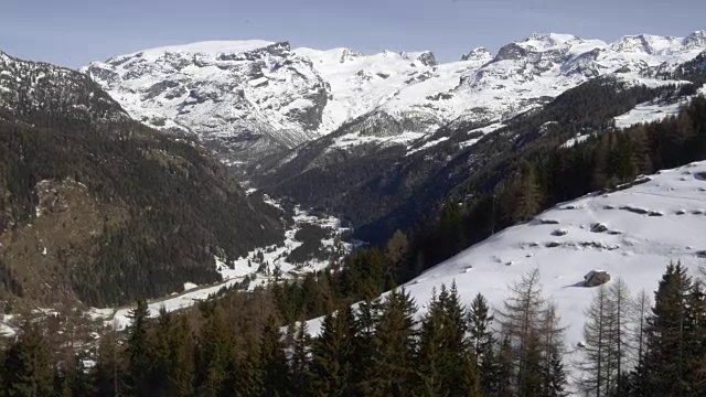 冬季无人机建立雪山下的森林森林山谷。雪山在户外自然。向后飞行。旅行探索阿尔卑斯山，4k俯视图视频