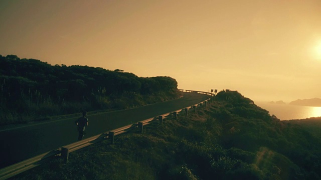 一名男子在柏油路上慢跑，山上可以看到日落时的大海
