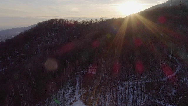 无人机在日落时分飞过白雪覆盖的森林，人们在散步。冬天的雪在野外的山中自然。阳光的光。旅行探索阿尔卑斯山，4k俯视图视频
