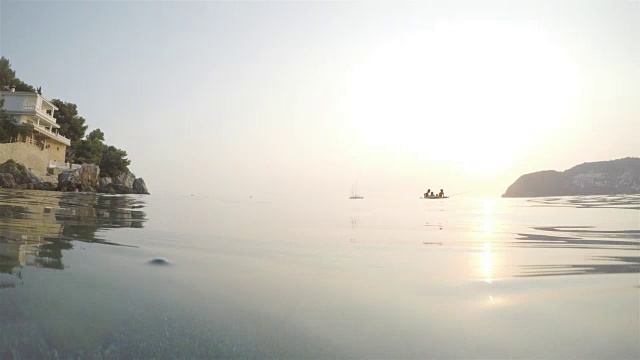 夕阳西下，三个男孩在海滩上钓鱼，摄像机半沉在水里