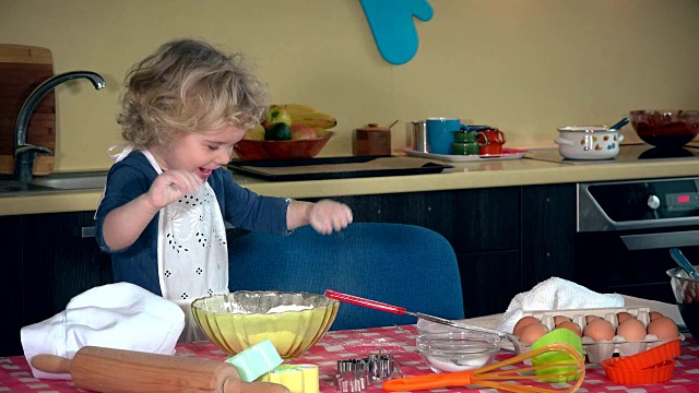 有趣的孩子玩面粉。女孩揉面团。女孩滑稽地沾上了面粉