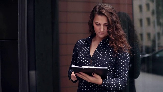 年轻有吸引力的商业女人看文件与严肃的看办公大楼附近