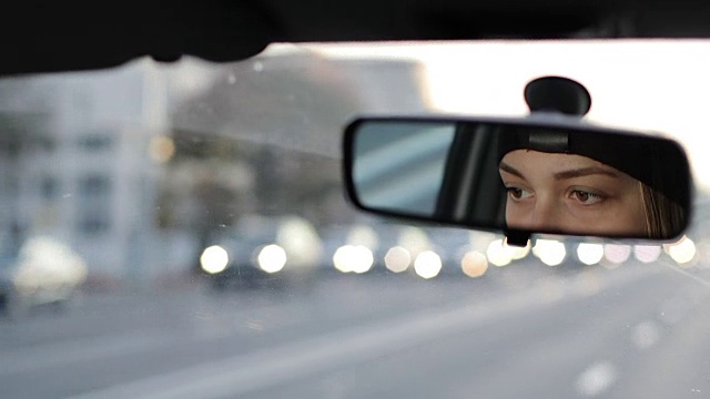 那个女孩正在开车。从汽车后视镜里可以看到女性的眼睛。