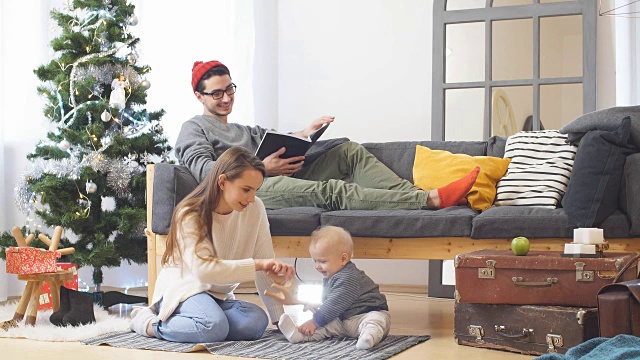 年轻快乐，阖家欢乐。妈妈、爸爸和小儿子穿着毛衣在家里的圣诞树和圣诞树旁玩耍，笑着、笑着。FullHD