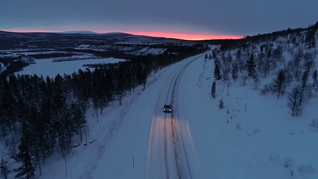 照片:日落时分，一辆汽车在雪山公路上穿过云杉林