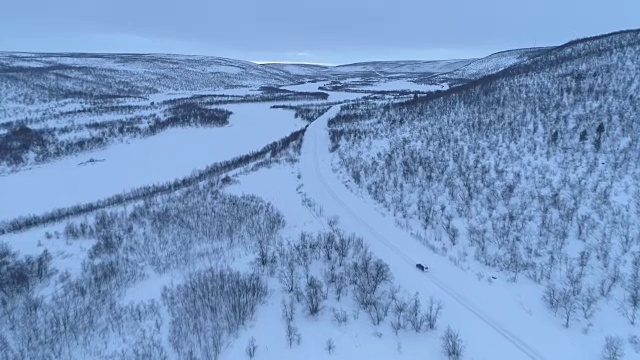 在冬天的早晨，一辆汽车在雪山脚下的高速公路上行驶