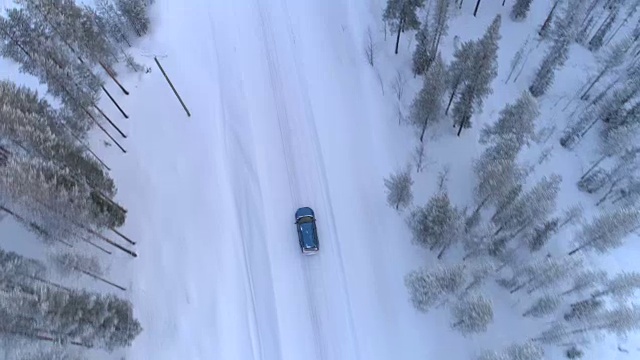 空中俯瞰:汽车行驶在积雪的道路上，穿过寒冷的冬季云杉森林