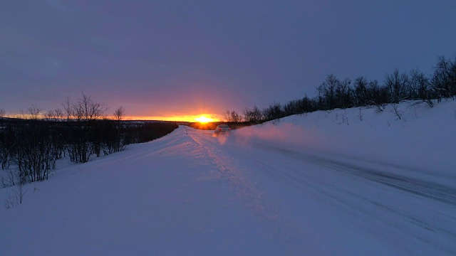 镜头:在冬日金色的夕阳下，高速汽车行驶在白雪覆盖的森林道路上
