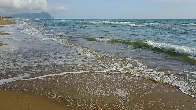 泡沫图案在沙滩的海浪和山的背景。航空摄影测量。慢动作