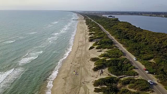 鸟瞰海边、海滩、道路、树木和水域下的蓝天。慢动作