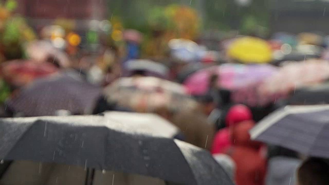 人们在繁忙的商业街撑着雨伞挡雨。真正的时间。人们在雨中带着雨伞上下班。模糊的散景。雨天的城市街道的自然背景