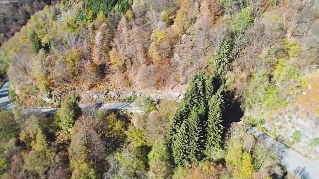 侧空中鸟瞰图，在彩色的秋天森林道路上行驶的黄色老古董汽车。秋天有橙、绿、黄、红的树林。山区街道道路的建立。4k无人机飞行建立商店