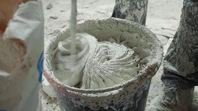 建筑工用电动搅拌机在桶中搅拌白色石膏。
