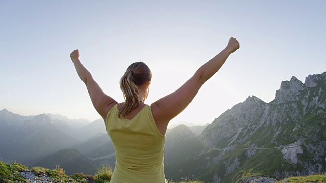 近镜头光晕:胜利的女人在令人惊叹的山顶上伸出手臂。