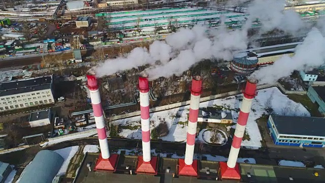 从火电厂的管道上飞过，蒸汽流到外面。城市建筑。空气污染。鸟瞰图。