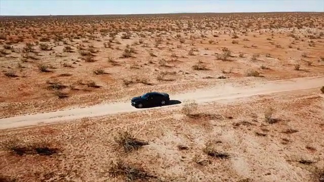 一辆黑色的汽车在沙漠的空旷道路上行驶。