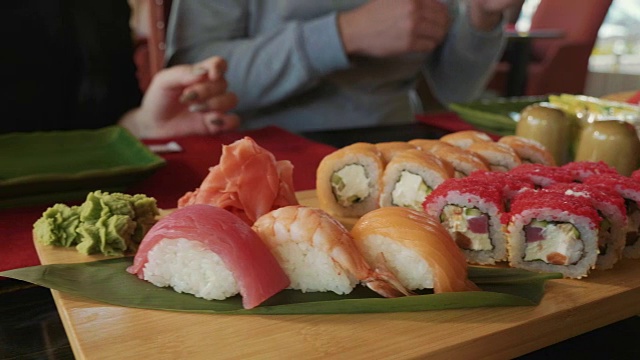 在一家日本餐馆里，一对年轻夫妇用筷子从盘子里拿寿司。