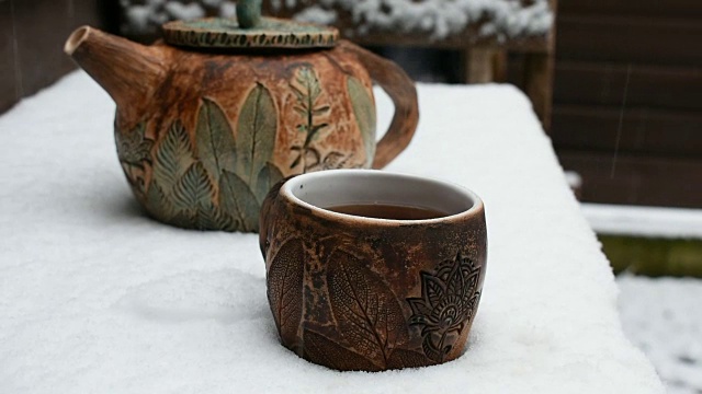 一个陶器茶壶和一杯热气腾腾的茶在飘落的雪