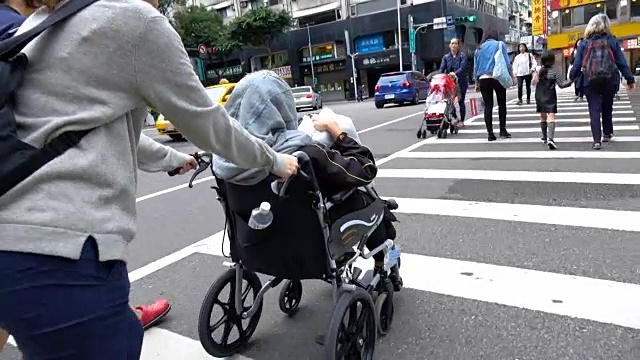 年轻女子推着轮椅上的老妇人过马路