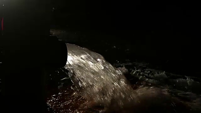 黑暗背光消防栓喷洒水到道路在晚上-近