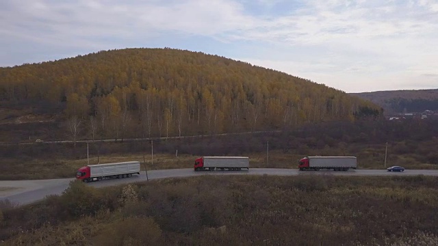 货车和汽车行驶在郊区的道路上，背景是秋天的森林