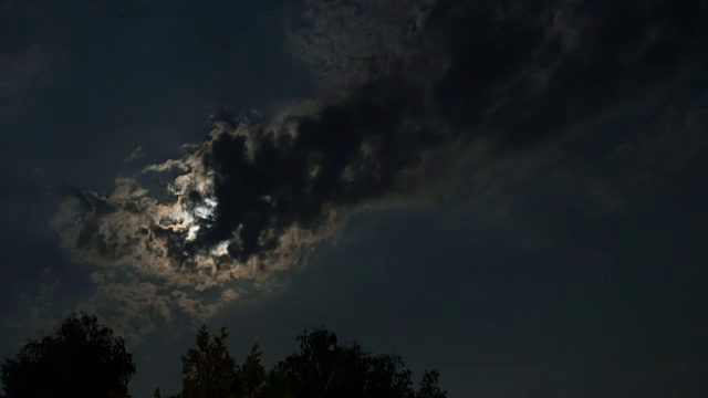 满月在夜空中穿过乌云和树木。间隔拍摄