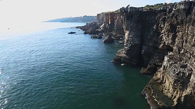 平静的海面和高高的岩石峭壁，轻浪翻滚，悬崖上的洞穴