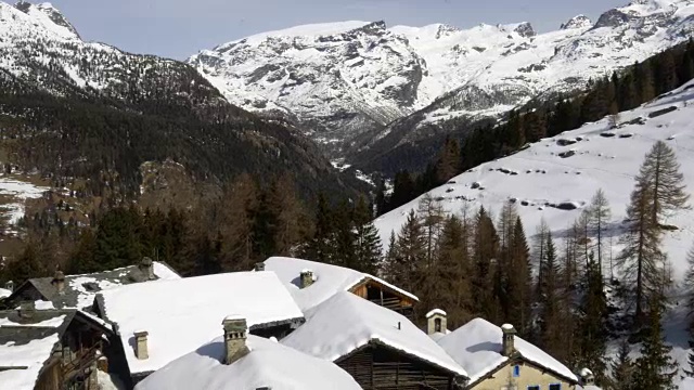 冬季无人机建立在雪山下的城镇和森林森林山谷。雪山在户外自然。一边飞行。旅行探索阿尔卑斯山，4k俯视图视频