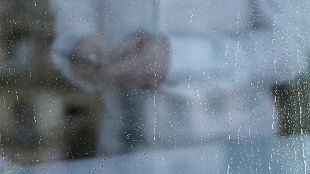 抑郁的离婚男人用智能手机发短信，雨水落在窗户玻璃上
