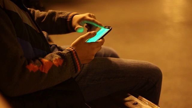 一个小男孩晚上在城市公园里拿着智能手机