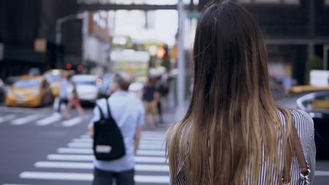 年轻美丽的女人在纽约过马路的背影，美国。女性看乘坐的汽车和出租车