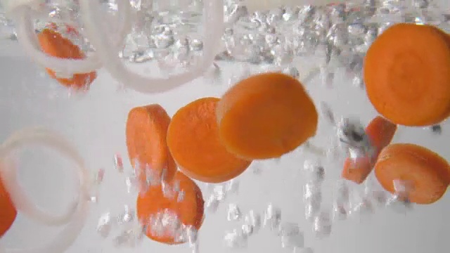 切成片的胡萝卜和洋葱圈落入沸水中。宏观视图