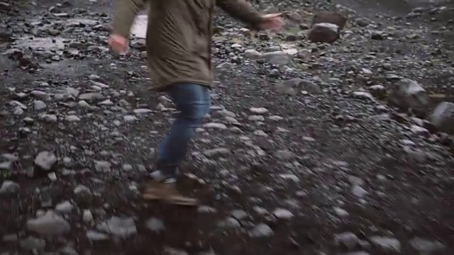 在冰岛的岩石路上，焦虑的男性脚穿着靴子从某人身边跑开的特写镜头