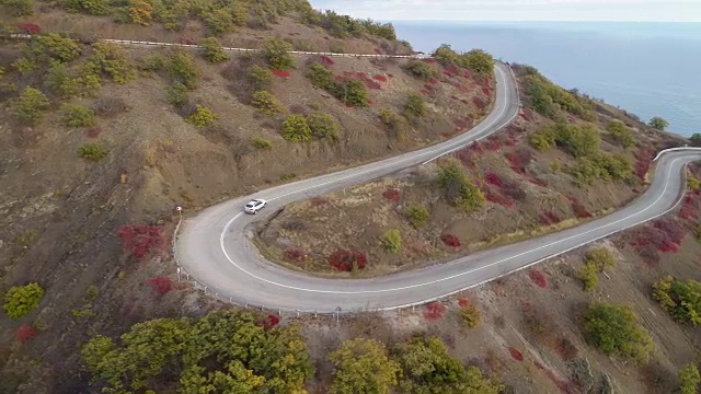 白色的跨界车在蜿蜒的山路上行驶。鸟瞰图。无人机在跟踪车辆。