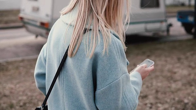 慢动作金发女人使用社交网络。后视图。女孩冲浪网站漫步秋天街道。生活方式拍摄