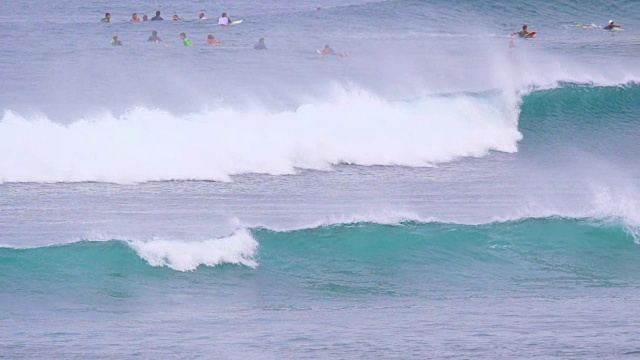 当冲浪者排成一列时，巨大的桶状海浪逼近海岸。