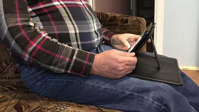 完整的人正坐在沙发上和平板电脑一起工作。他不时地用手指触碰屏幕。