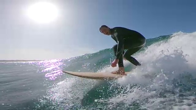 慢镜头，镜头光晕:兴奋的冲浪运动员微笑着，骑着波浪向海岸走去。